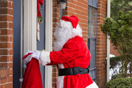 Santa Claus of carrying a big bag christmas gift delivery outdoors, near houseの写真素材