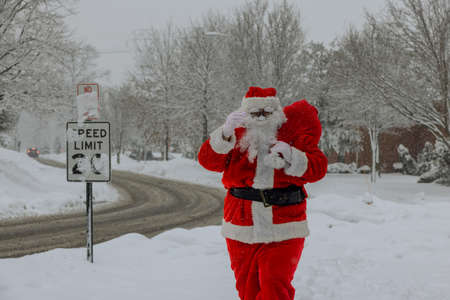 Snow Santa Claus walking along the street carries a large bag of gifts on trees covered with snowの写真素材