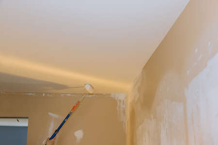 Rear view of painter paints the ceiling with a rollerの写真素材