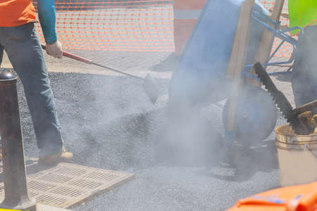 Road worker repair asphalt covering new road surface while laying asphaltの写真素材