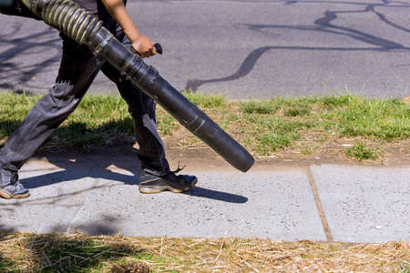 The gardener cleans up the park path leaf blower with garden tools for generating air flow.の写真素材