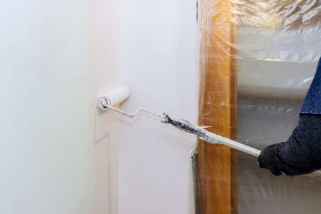 Rear view of painter paints the wall with a roller in roomの写真素材