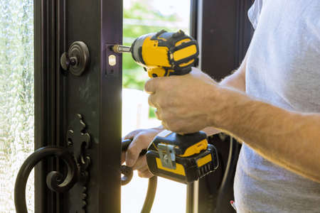 Builder in installing a door lock the door of a new house hand close-up.