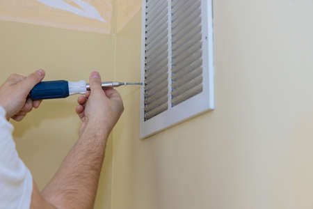 Removing air vent cover on wall with square but screw driver on the wallの写真素材