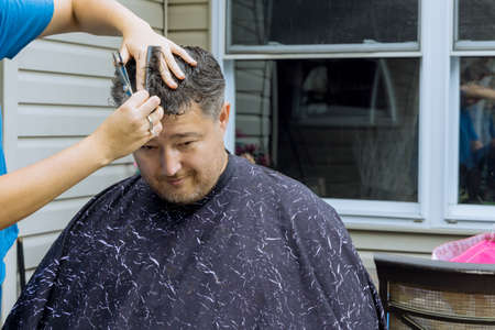Professional barber with man getting haircut while sitting in chair at home outsideの写真素材