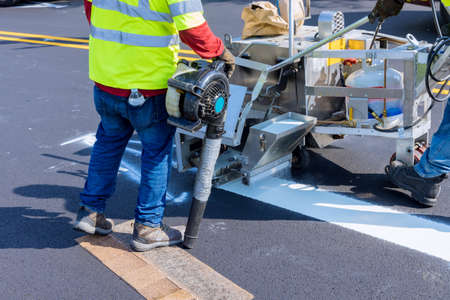 Road construction worker painting white line on the street surface tor thermoplastic spray marking machine during road constructionの写真素材