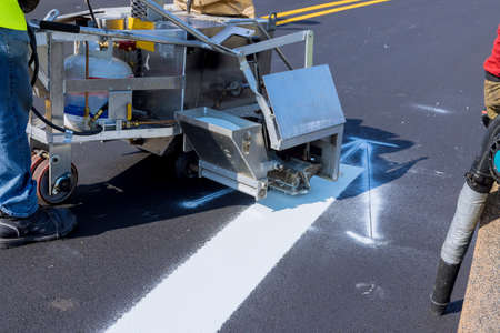 Workers apply white paint a road marking the stripes with a reflective powder on the new asphaltの写真素材