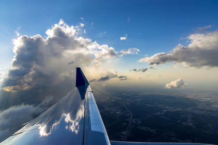 Flight wing of plane over dramatic white fluffy clouds on blue sky during sunset.の写真素材