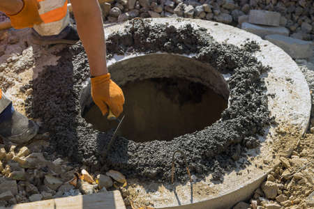 Construction worker installation of sewerage a sewer manhole on septic tank with connection to central streetの写真素材
