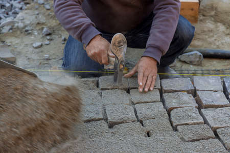 Paving pavement with granite stones, workers using industrial cobblestones for paving road with...