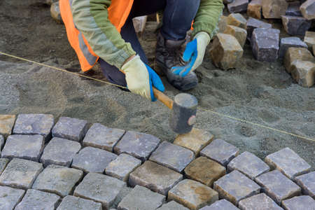 Worker using rubber hammer to build stone sidewalk of installing laying pavement stones on sidewalk near road in cityの写真素材