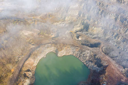 Misty landscape open pit stone extraction in the canyon with deep green lake with mountain peaks in morning fog on aerial viewの写真素材