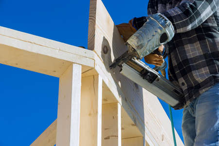 A carpenter for nailing wooden beam using an air hammer on construction site