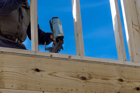 Builder in nailing wooden beams works for construction using an air hammer of housing development