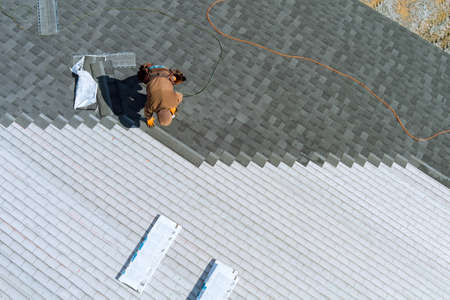 A worker installing shingles on the roof of a home with air hammer and nailsの写真素材