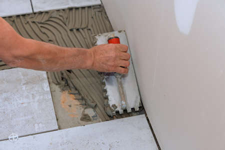Home construction working with master puts adhesive base over floor for ceramic tile