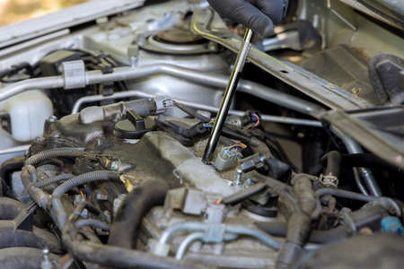 A man unscrews an old spark plug from a car engine with using special tools in garage service