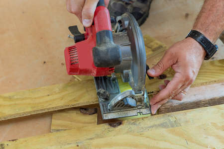 Carpenter cutting with a hand electric saw the wooden board