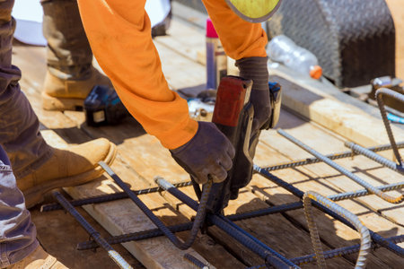 Construction worker hands twisting reinforcement securing steel bars with wire rods for cement...