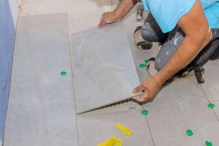 Placing ceramic tiles on glue-smeared floors using tile adhesive in construction worker tiling