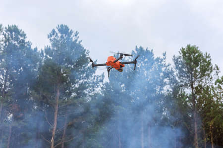In ecological disaster follow a fire through the forest trees with a drone, the fire department uses an aerial cameraの写真素材