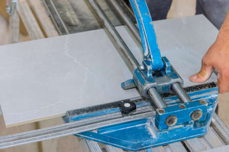 On a ceramic tile floor, a construction worker uses a manual tool to cut the tiles and lay them with the help of the equipment during bathroom renovationの写真素材
