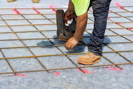 Construction worker twist steel bars with wire rod reinforcement into cement foundations using tool known as the rebar tying toolの写真素材