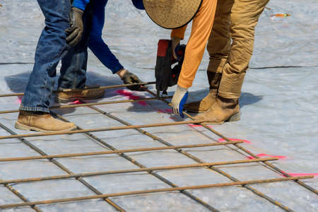 As part of the cement foundation construction process, a construction worker uses rebar tying tool...