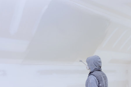 Using a spray gun and primer, worker paints the walls and ceiling of new houseの写真素材