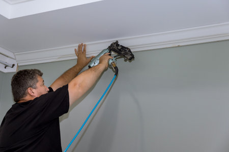 During the construction of newly constructed home, this carpenter was nailing wooden crown molding between ceiling and wallの写真素材