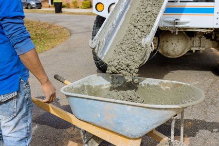 Mixer truck pours concrete into wheelbarrow at construction siteの写真素材