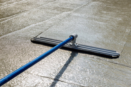 This worker holding steel fresno trowel and smoothing out new sidewalk on newly poured sidewalk,...