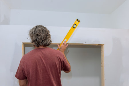 Before drywall is painted employee checks level of drywall with aid level