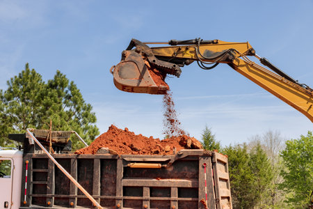 Excavator is scooping up soil in dumper truck is waiting to be loadedの写真素材