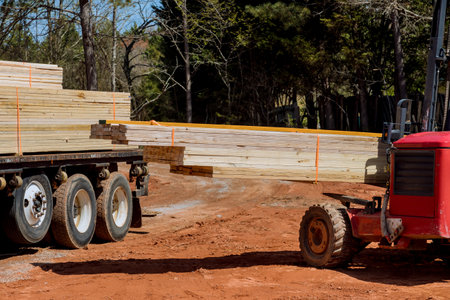 An operator of lift manipulator unloads wooden building material delivered to construction site...