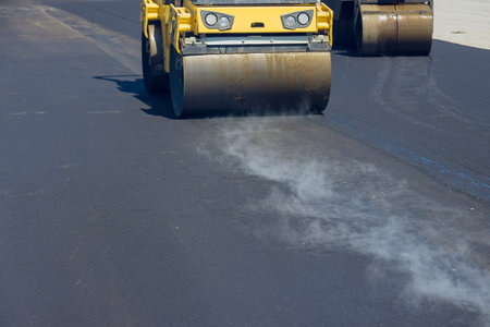 During vibratory road roller compactor process construction worker is operating machine that lays new asphalt on roadの写真素材