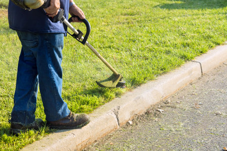 Municipal worker lawn mower close to road mows fresh green grass with hand mower
