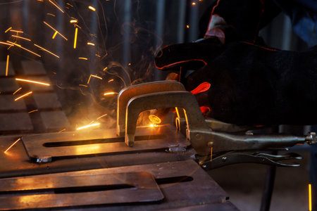 Heavy industry worker in protective mask welds steel and other products in factory environment...