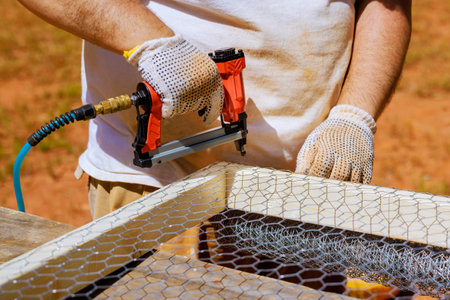 With help of nail gun worker nails metal mesh to wooden frameの写真素材