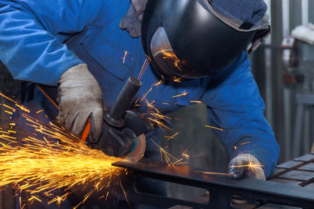 During metalwork workplace in which master grinds metal with grinder sparks are visible throughout factory as he worksの写真素材