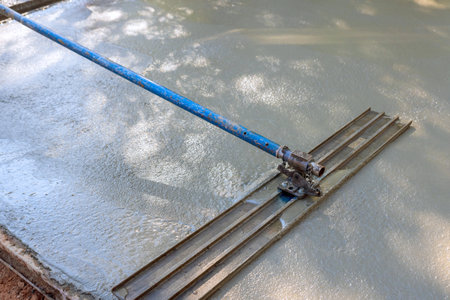 Concrete for driveway is being leveled by workers on construction site using mix concrete trowels