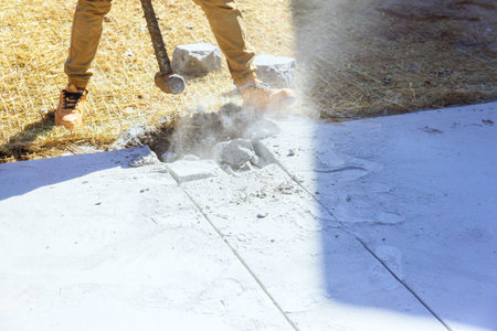 Hammer wielding worker breaks concrete old driveway at construction siteの写真素材