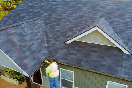 Worker cleans clogged roof gutter drain from dirt debris, as well as fallen leaves that have fallen
