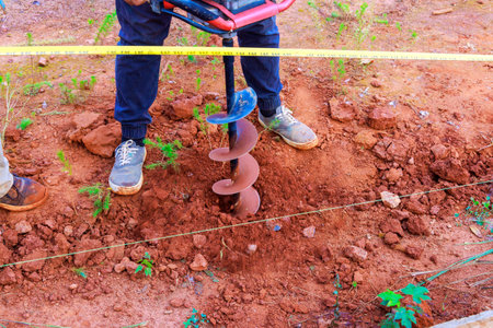 Worker digs ground with1 gasoline drilling machine in for fence postsの写真素材