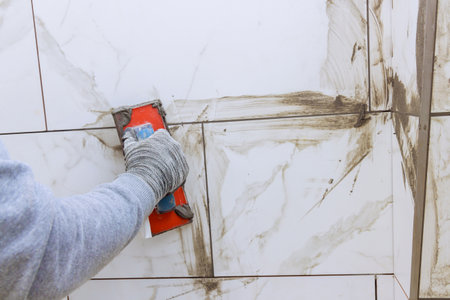 Grouting ceramic tiles with tilers filling space between tiles using rubber trowel.の写真素材
