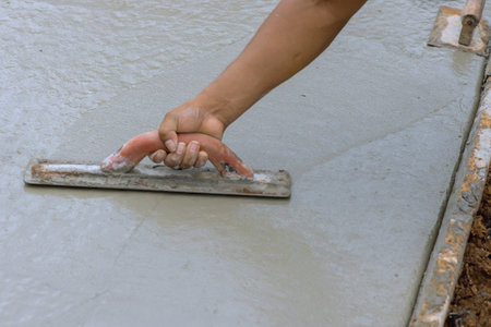 Worker leveling fresh concrete pavement with wet cement using special working toolの写真素材