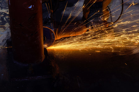 Worker cuts metal with abrasive disk in industrial factory with sparks while grinding ironの写真素材