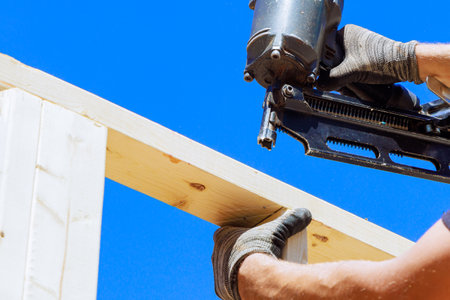 Worker in holding plank installing it on household construction using air hammer in nailing wooden beams.の写真素材