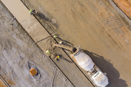 Concrete is poured from mixer truck for construction of pedestrian walkway by masonry workersの写真素材
