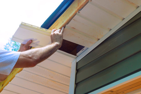 Installing vinyl soffit plastic panels on facade ceiling of new house by an employee